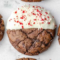 a chocolate cookie with white frosting and sprinkles on top, surrounded by other cookies