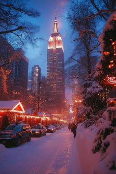 a city street covered in snow with cars parked on the side and buildings lit up at night