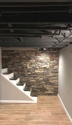 an empty room with stone walls and white stair railings, in front of a brick wall