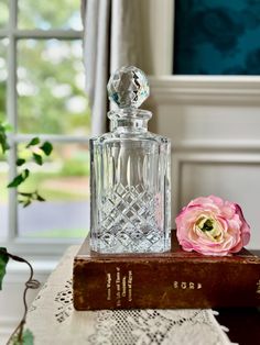 a glass bottle sitting on top of a wooden table next to a book and pink flower