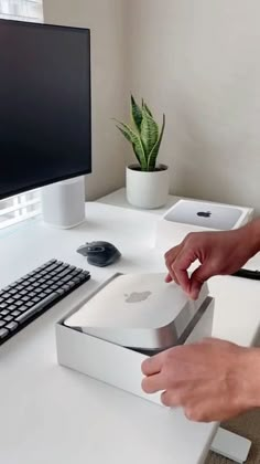 a person opening an apple computer box on a desk next to a keyboard and monitor