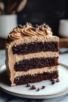 a slice of chocolate cake with frosting and chocolate chips on a plate next to coffee beans