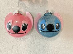 two ornaments hanging from the wall with faces painted on them, one pink and one blue