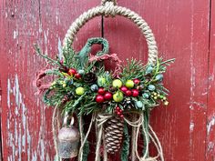 a christmas wreath hanging on the side of a red door with pine cones and berries