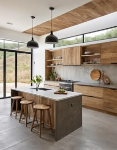 a kitchen with wooden cabinets and stools next to an open floor plan that has sliding glass doors