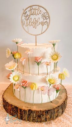 a three tiered cake with flowers on the side and a wooden sign that says, little wildflowers