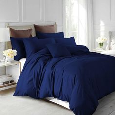 a bed with blue sheets and pillows in a white room next to a window,