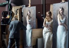 a woman in a white dress standing next to three canvases with pictures on them