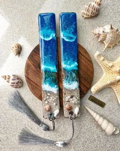 two blue glass candles sitting on top of a wooden plate next to shells and seashells