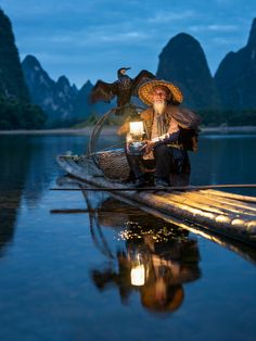 a man sitting on top of a boat with a bird perched on his arm and holding a lantern