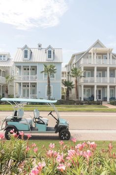 a golf cart is parked in front of some white houses with pink flowers and palm trees