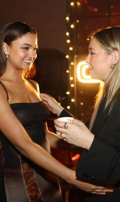 two beautiful young women standing next to each other in front of a neon light sign