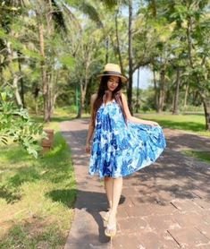 a woman in a blue dress and hat walking down a path