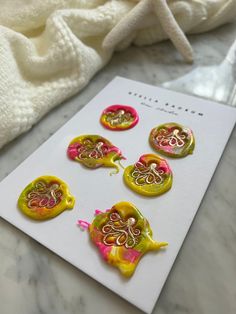 six yellow and pink buttons sitting on top of a white card next to a towel