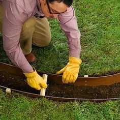 a man in yellow gloves is working on a garden bed with wood planks and grass