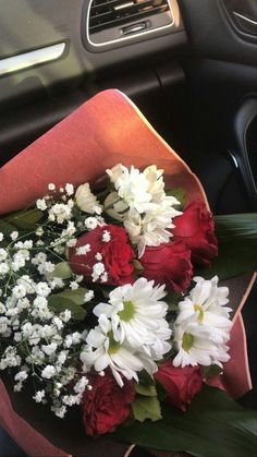 a bouquet of white and red flowers sitting on top of a car dash board in the passenger seat