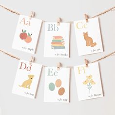 there are many cards with animals and letters on them hanging from clothes pins in front of a white wall