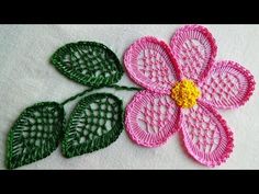 a crocheted flower and two leaves on a white tablecloth with green trim