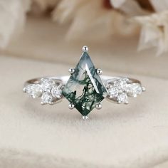 a green and white diamond ring sitting on top of a table next to some flowers