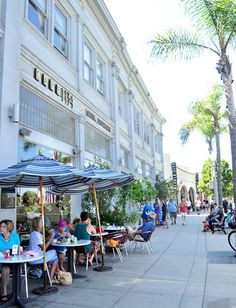 people are sitting at tables under umbrellas on the sidewalk in front of a building