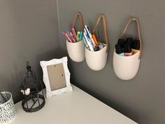 three white buckets hanging on the wall above a desk with pens and pencils