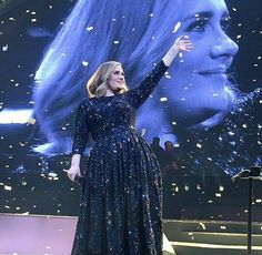 a woman in a blue dress is on stage with her arms up and hands out