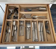 a drawer filled with silverware and utensils on top of a wooden table