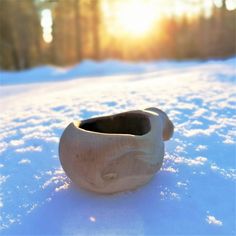 a wooden bowl sitting in the snow with trees in the background and sun shining through