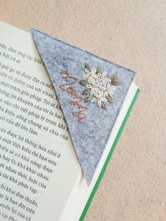 an open book with a felt flower on it and a small triangle shaped brooch