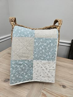 a blue and white patchwork pillow sitting on top of a wooden table next to a wicker basket