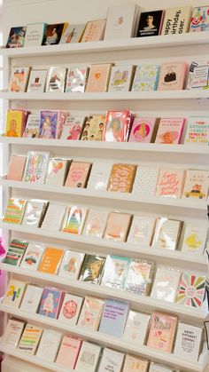 many cards are displayed on the wall in front of bookshelves and vases