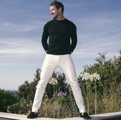 a man in black shirt and white pants standing on ledge with his hands behind his back