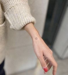 a woman's hand with a tiny star tattoo on her left wrist and red nail polish