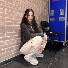 a woman sitting on the ground in front of a brick wall with her headphones up