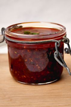 a glass jar filled with red sauce sitting on top of a wooden table next to a knife