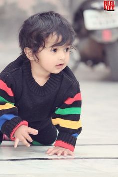 a small child crawling on the ground in front of a parked car and looking at the camera