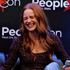 a woman sitting down laughing and holding a cell phone