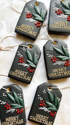 four tags with merry christmas written on them hanging from twine string and decorated with holly berries