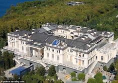 an aerial view of a large white mansion in the middle of some trees and water