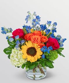 a vase filled with colorful flowers and greenery on a white background, in the center is an orange sunflower surrounded by blue and red roses