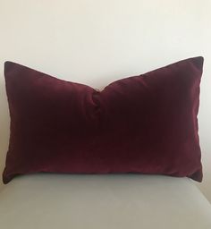 a dark red pillow sitting on top of a white couch next to a wall with a light fixture