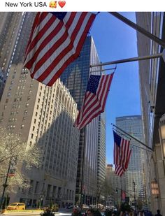 several american flags flying in the air near tall buildings on a city street with skyscrapers