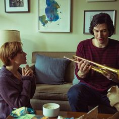 a man and woman sitting on a couch playing musical instruments in front of each other