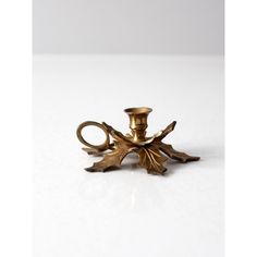 an antique brass candle holder with leaves on it's sides and a single candle in the middle