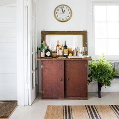 a room with a clock on the wall next to a cabinet and potted plant