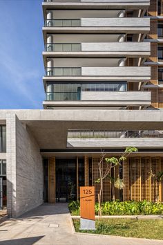 an apartment building that is very tall and has plants growing in the front garden area