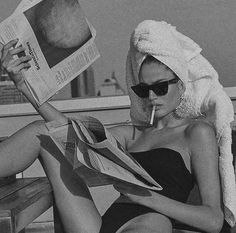 a woman with a towel on her head is reading a paper while sitting on a bench