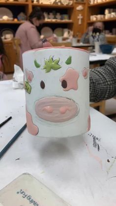 a mug with a cow painted on it sitting on a table in a room full of people