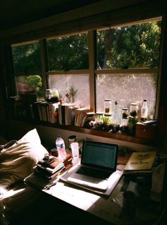 a laptop computer sitting on top of a desk in front of a window filled with books