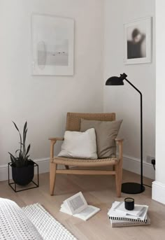 a living room with a chair, lamp and books on the floor in front of it